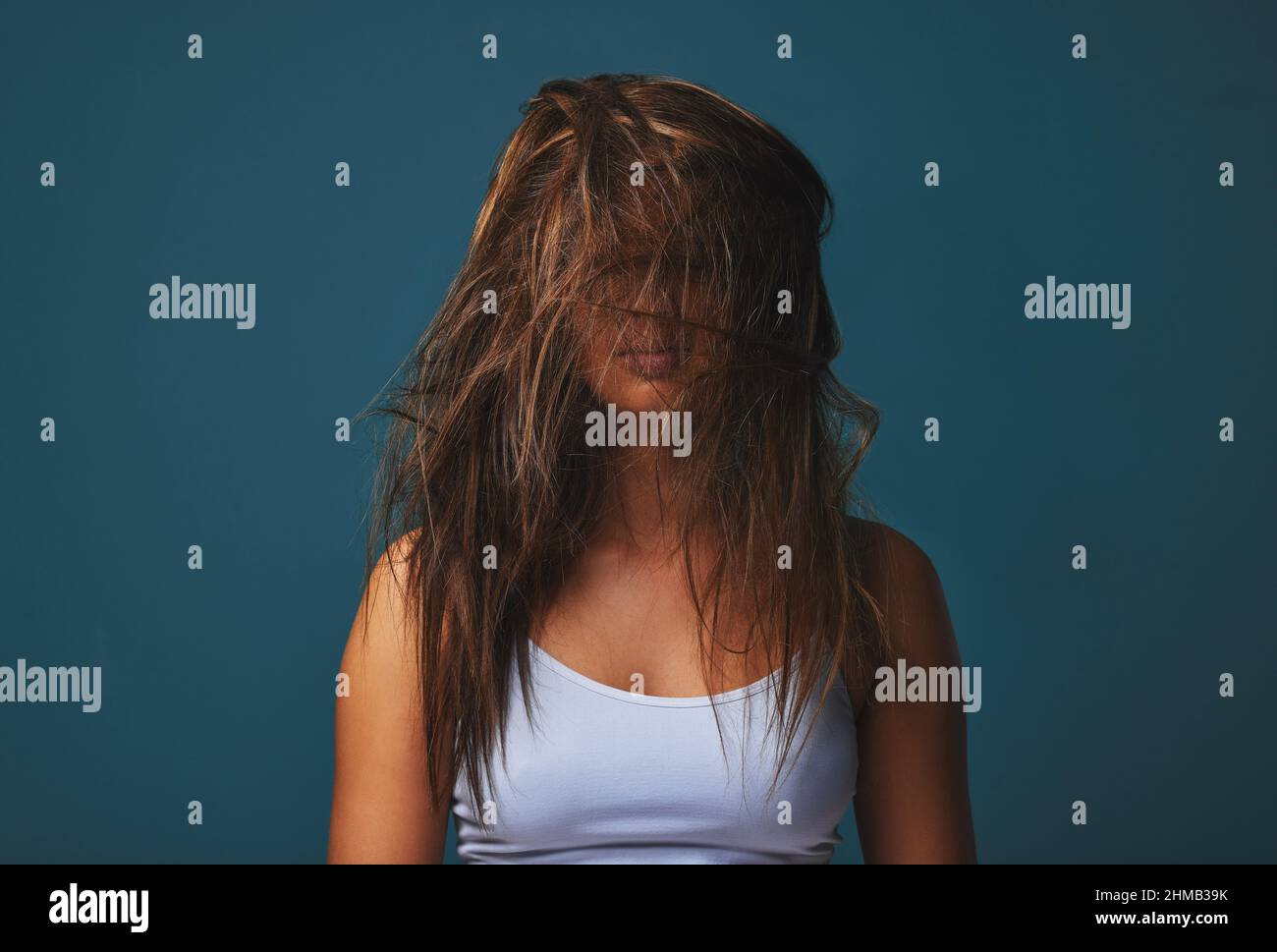 Il suo tutto sudicio. I capelli, il letto, le parole, persino il cuore. Studio girato di una giovane donna che copre il suo viso con i capelli che posano su uno sfondo blu. Foto Stock
