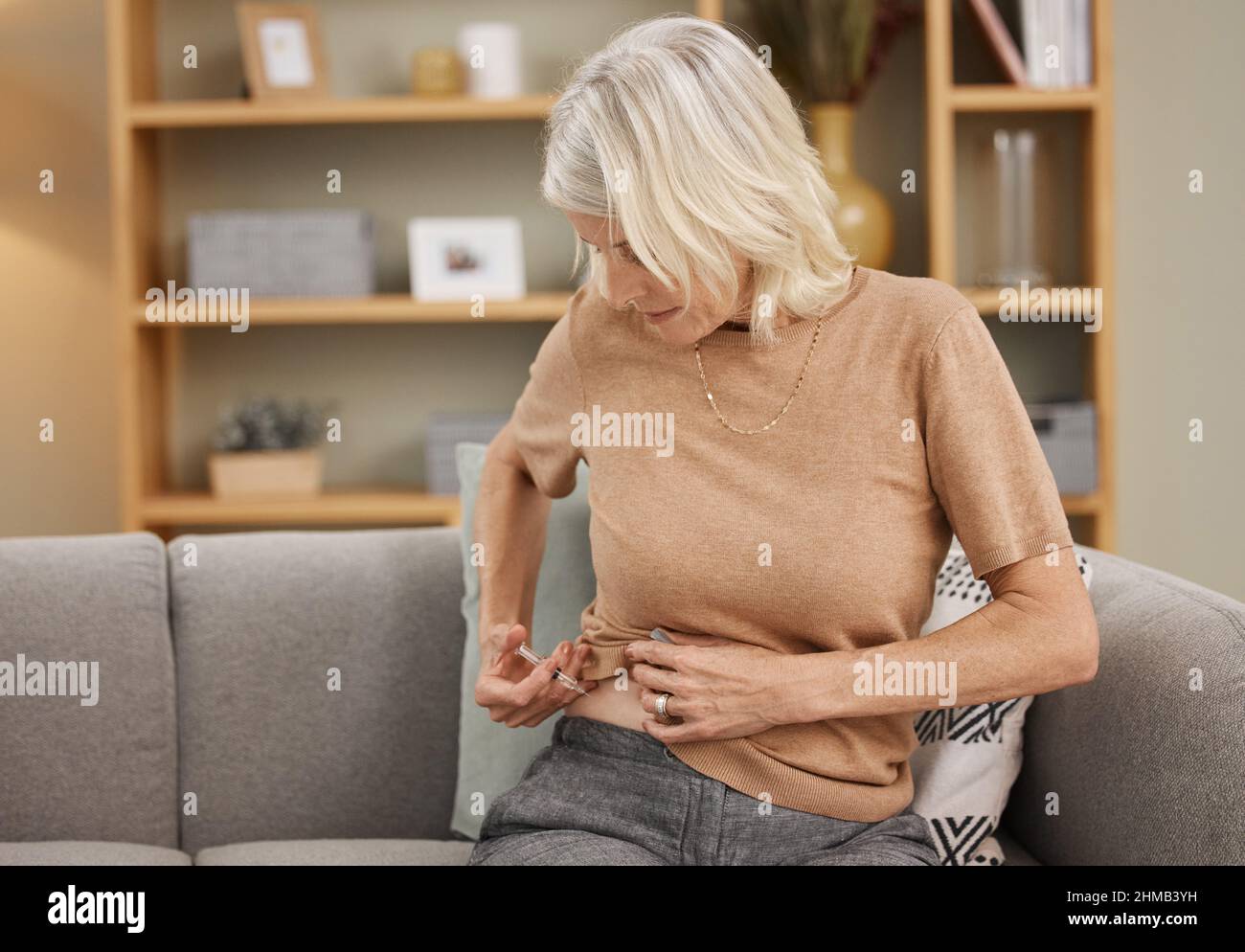 Un colpo un giorno mantiene il diabete via. Shot di una donna matura che si inietta con insulina sul divano a casa. Foto Stock