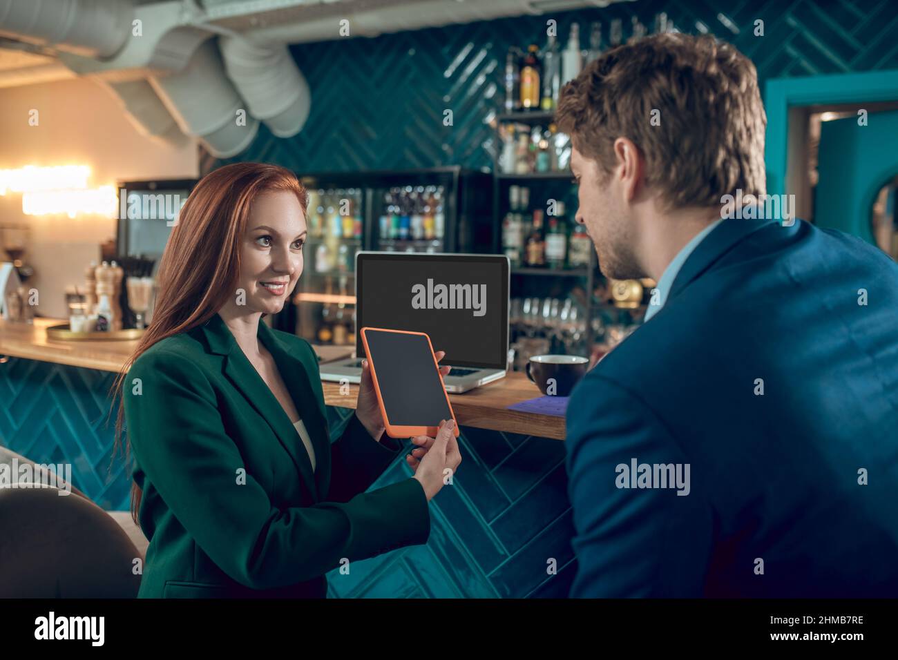 Donna che mostra lo schermo del tablet a un uomo seduto in un bar Foto Stock