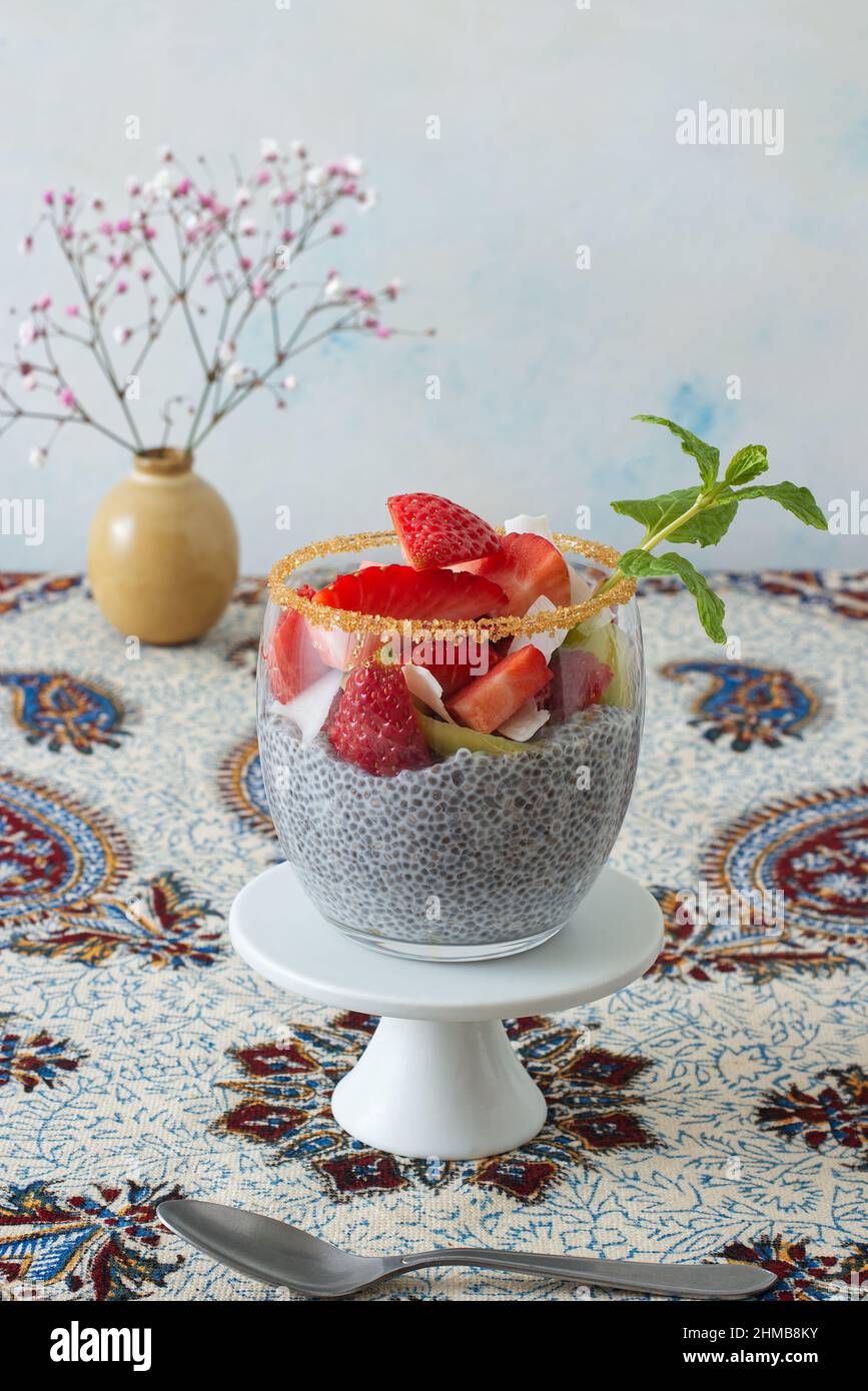 Vista ad angolo basso del dessert chia budino con bacche estive, fragole, kiwi e fette di cocco, impreziosito da un rametto di menta. Nessuna gente. Foto Stock