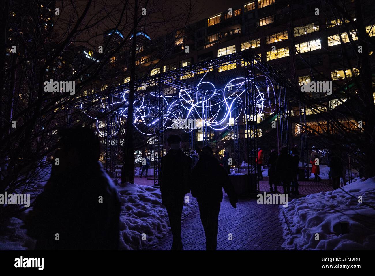 Toronto, Canada. 07th Feb 2022. La gente esce da un'installazione artistica all'aperto 'Pressure' di Hans E. Madsen e Frederik D. Houds, un pezzo costituito da una serie di 300 metri di luci a LED RGB pulsanti che assomigliano a un doodle, avvolto intorno a una grande costruzione. La mostra invernale Nordic Lights Outdoor è una mostra di arte leggera nordica e canadese presso il Toronto Harbourfront Centre, co-prodotto con Fjord Studio. Credit: SOPA Images Limited/Alamy Live News Foto Stock
