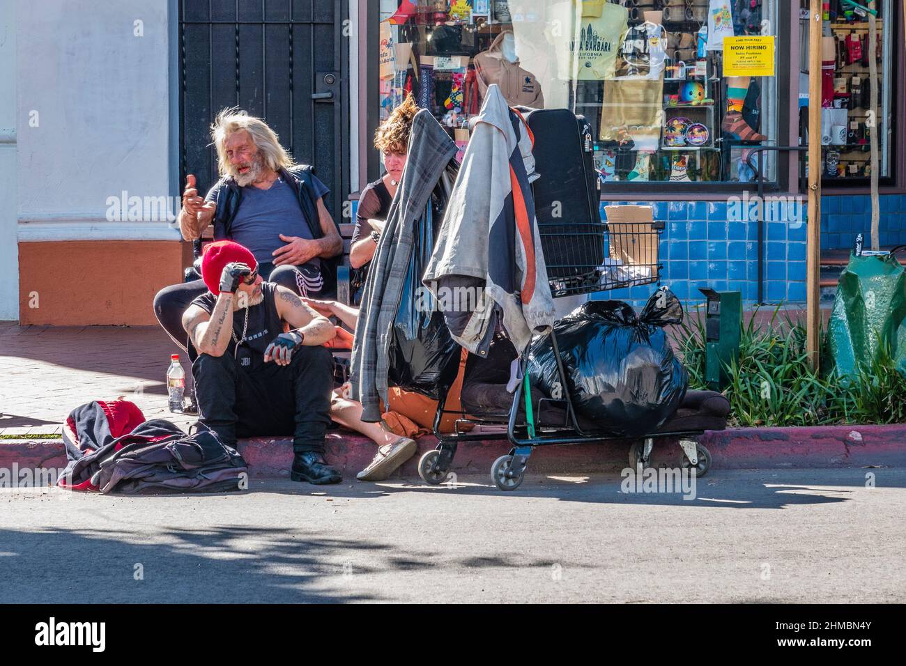 Tre senzatetto, due maschi e una femmina, seduti sul marciapiede e a marciapiede su state Street con i loro beni mondani e un carrello della spesa. Foto Stock