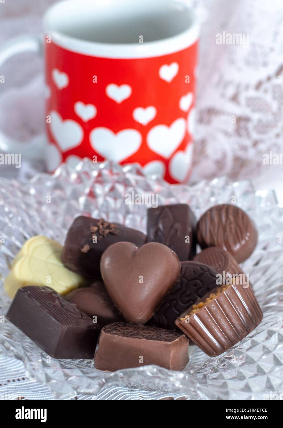 Un piatto di caramelle fantasia contiene cioccolatini gourmet per il vostro valentine, e una tazza graziosa rossa e bianca con cuori vi mostrano la cura Foto Stock