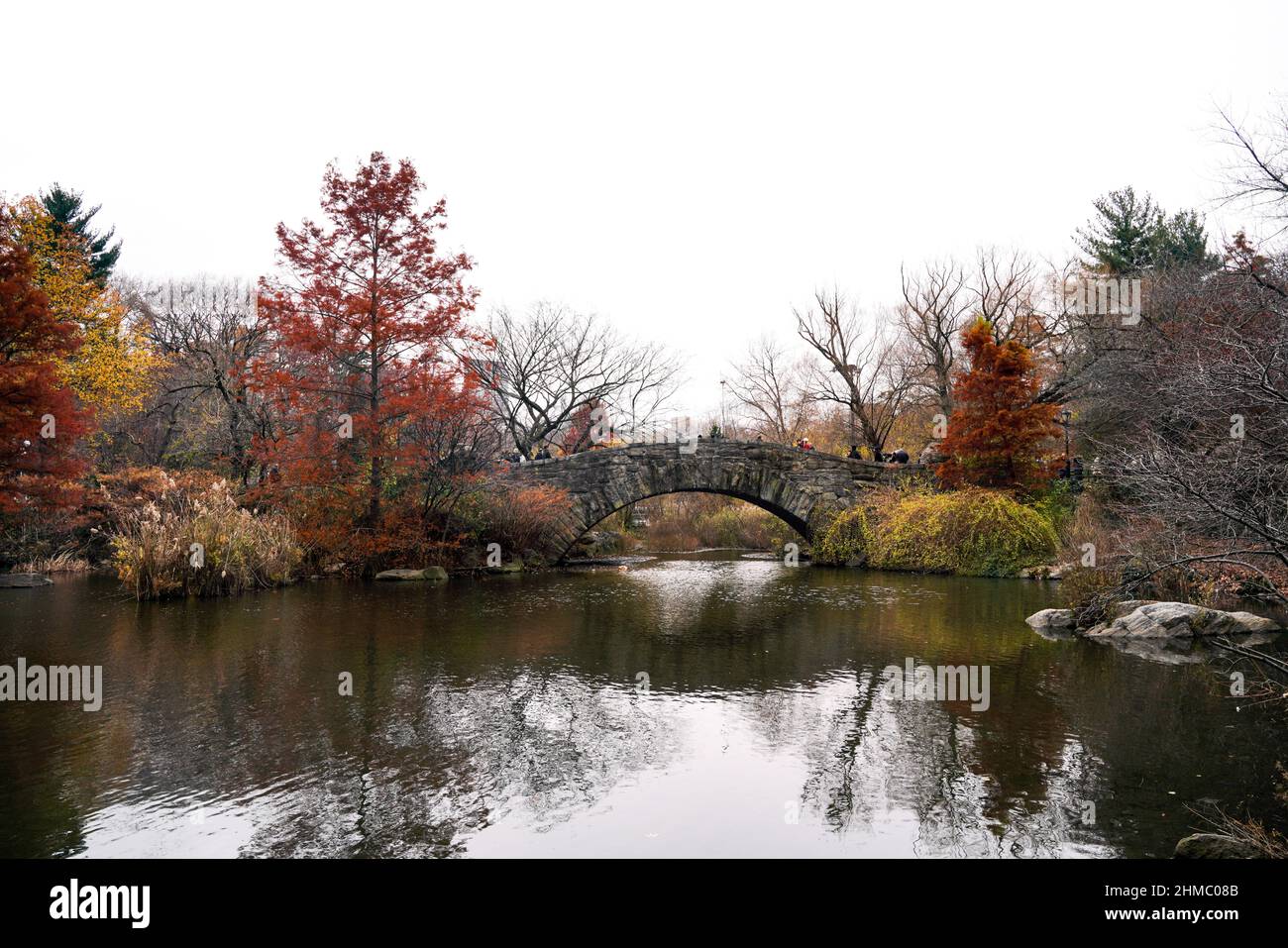 Il fogliame autunnale e l'iconico Gapstow Bridge si affacciano sullo stagno e sul santuario naturale di Hallett nell'angolo sud-orientale di Central Park, New York. Foto Stock