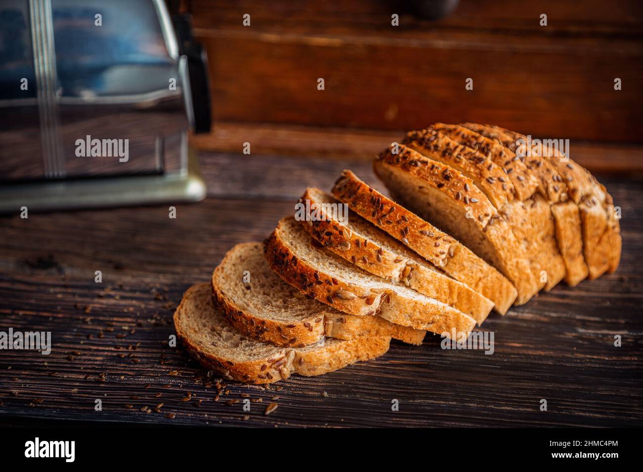 Pane fresco di lino di frumento intero e semi di girasole affettato su un rustico tavolo di legno con scatola del pane e spazio per la copia. Foto Stock