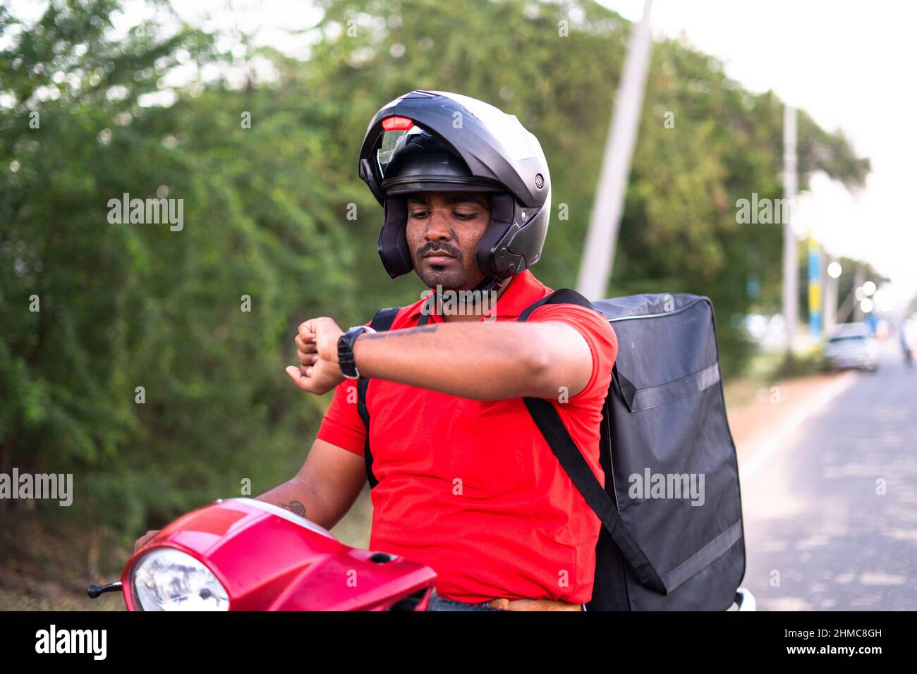 Preoccupato il delivey indiano su scooter a causa di ritardo delivey servizio - concetto di stressante stile di vita di lavoro, occupazione e servizio di corriere. Foto Stock