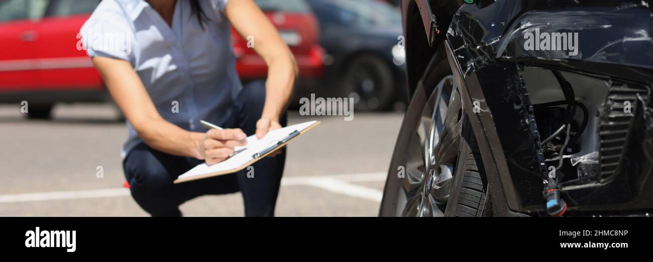 Ispettore donna che scrive in documenti su appunti vicino auto rotta. Assicurazione auto Foto Stock