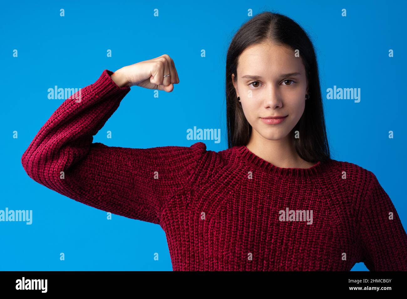 Bella giovane donna che mostra la sua muscolarità e guardando la macchina fotografica su sfondo blu Foto Stock