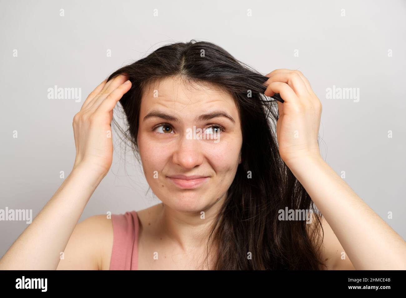Una bella donna bruna senza trucco con capelli sporchi oleosi tiene le mani sulla testa con uno sguardo insoddisfatto Foto Stock