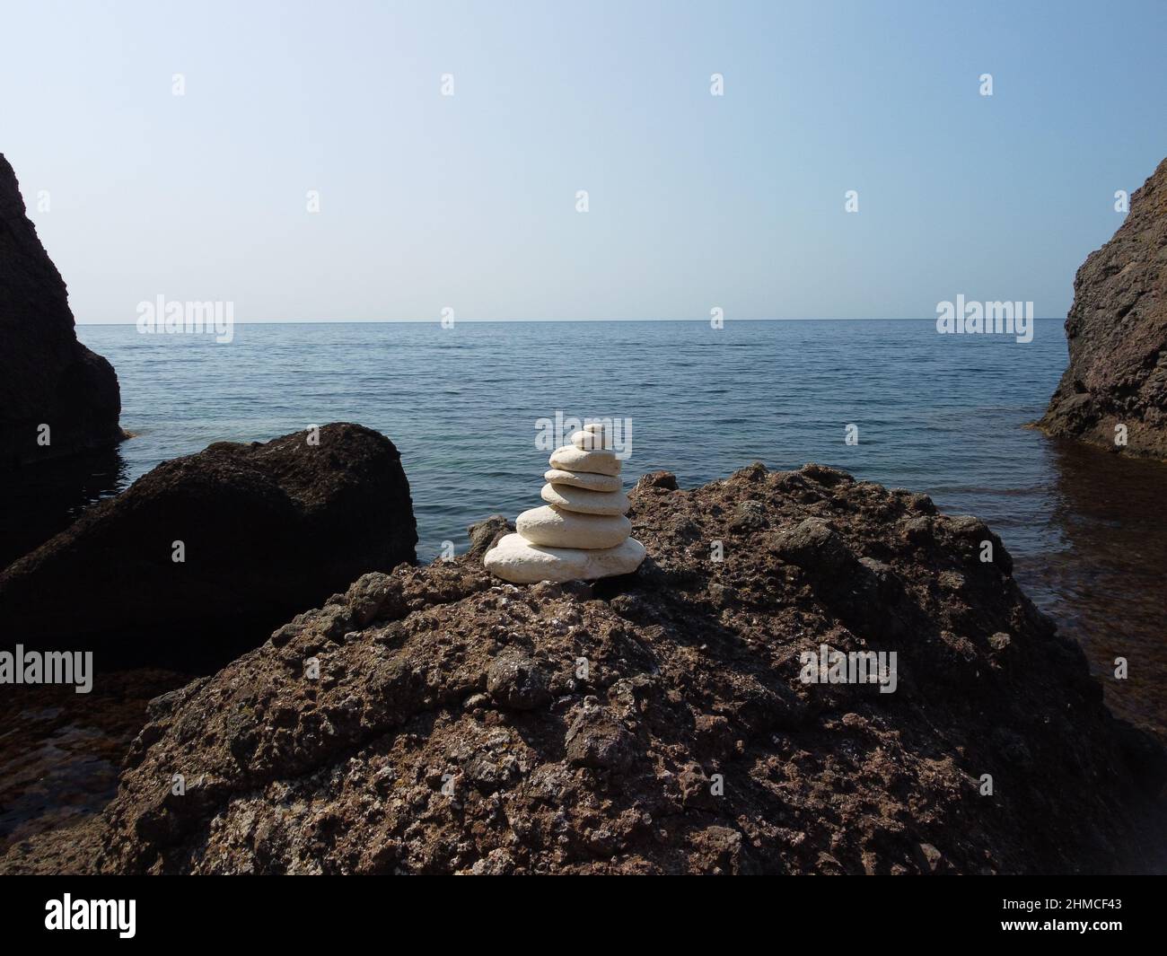 Piramide di ciottoli bilanciata sulla spiaggia nelle giornate di sole e cielo limpido al tramonto. Il mare d'oro bokeh sullo sfondo. Fuoco selettivo, pietre zen sulla spiaggia di mare Foto Stock