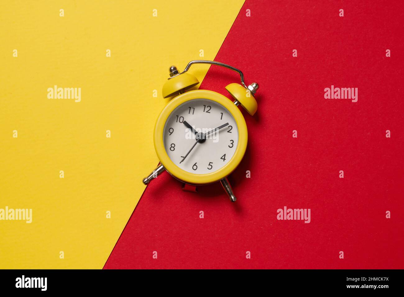Sveglia gialla su sfondo giallo, blu, rosso e verde. Spazio di copia. Concetto di tempo. Foto Stock
