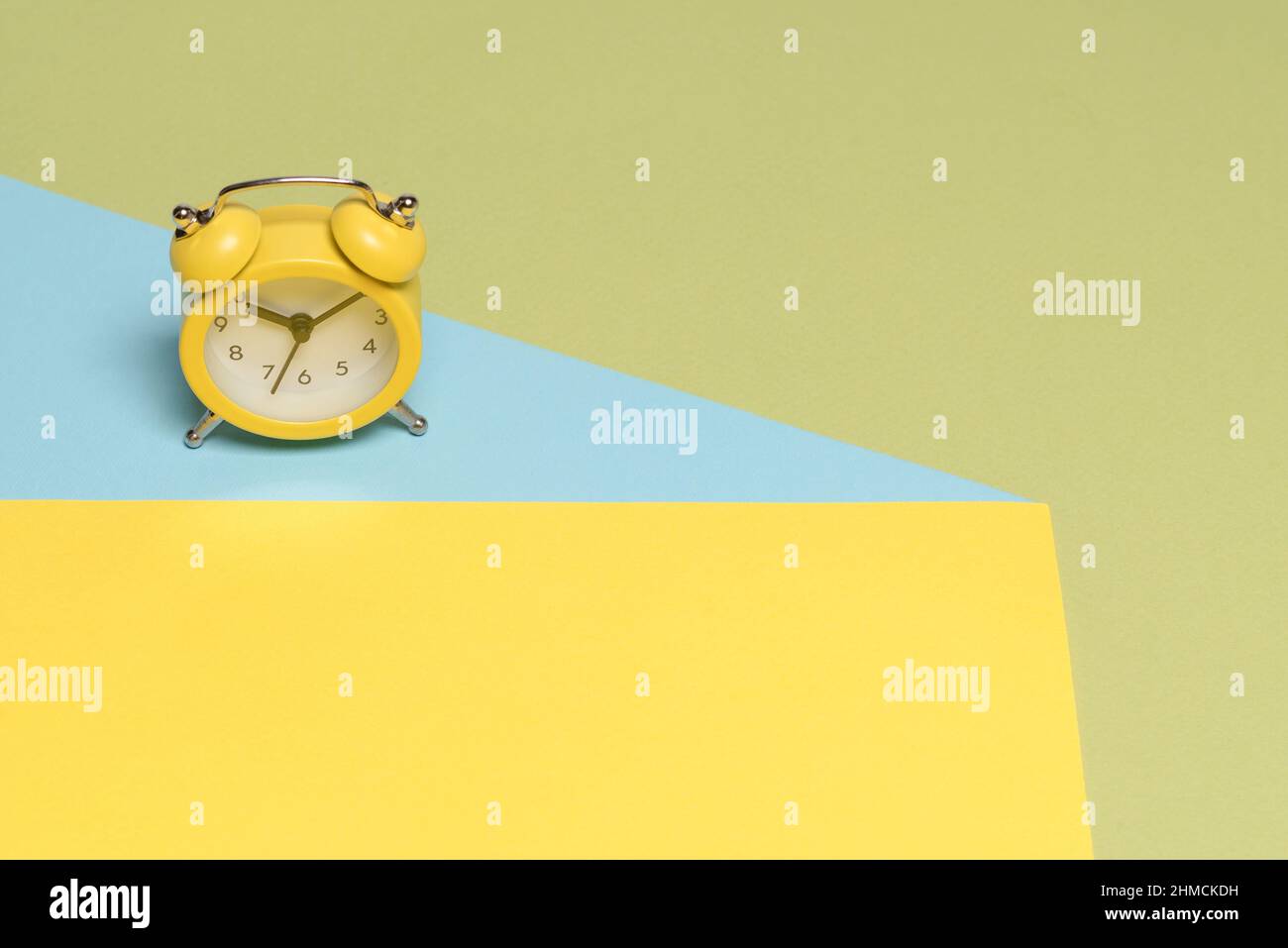 Sveglia gialla su sfondo giallo, blu e verde. Spazio di copia. Concetto di tempo. Foto Stock