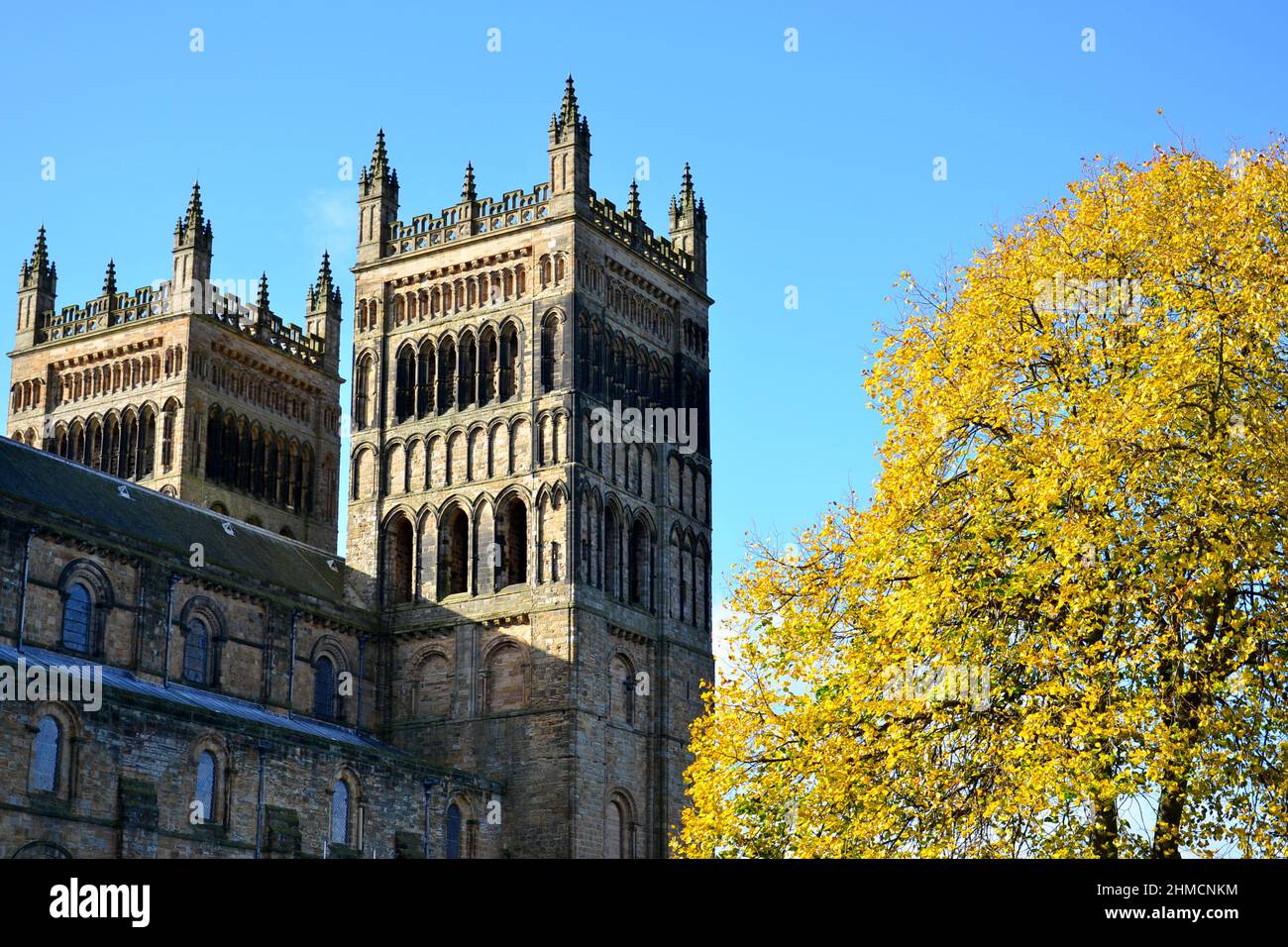 Primo piano delle maestose torri della cattedrale di Durham contro un profondo cielo blu e alberi dorati all'esterno in una giornata di sole Foto Stock