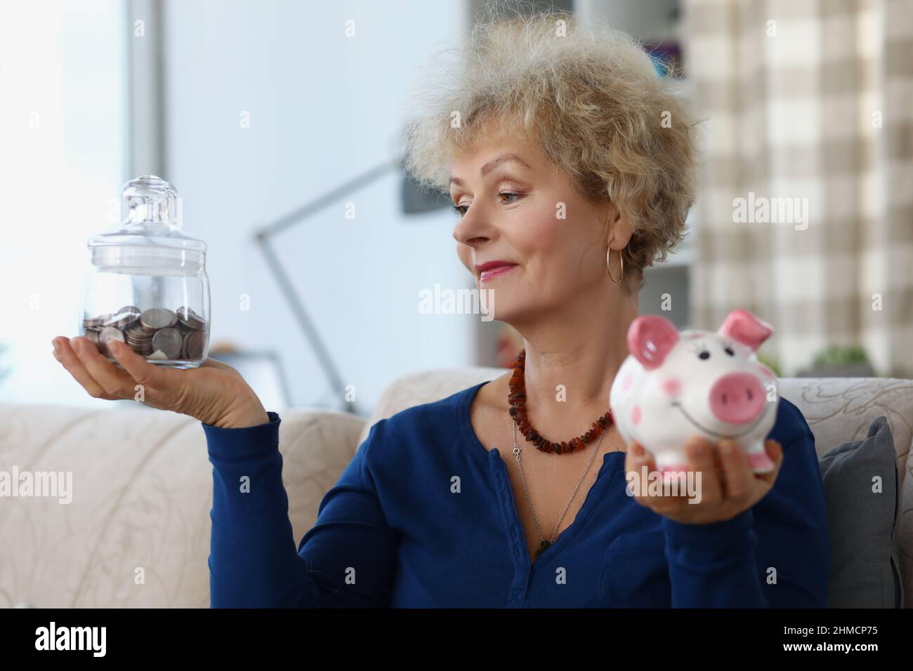 Donna anziana tenere contenitore di vetro con soldi risparmiati per la pensione e piggybank Foto Stock