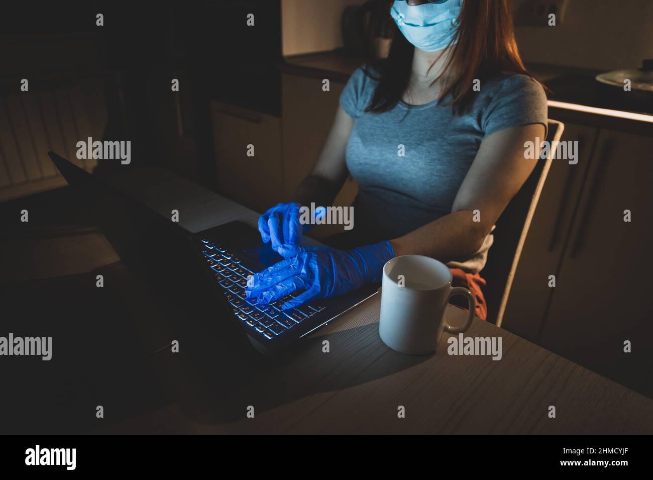 Una ragazza in una maschera e guanti impara durante la quarantena. Una donna che lavora fuori orario da casa su un notebook. Un freelance è seduto in cucina nel Foto Stock