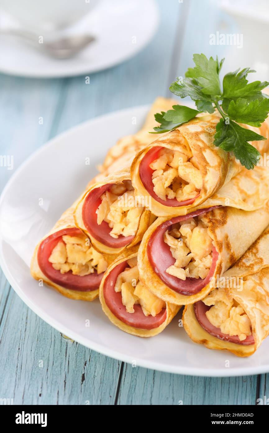 Pancake fatti in casa sottili con una fetta di prosciutto e uova strapazzate, impilati in una pila, sul tavolo. Ottima idea per la colazione. Foto Stock