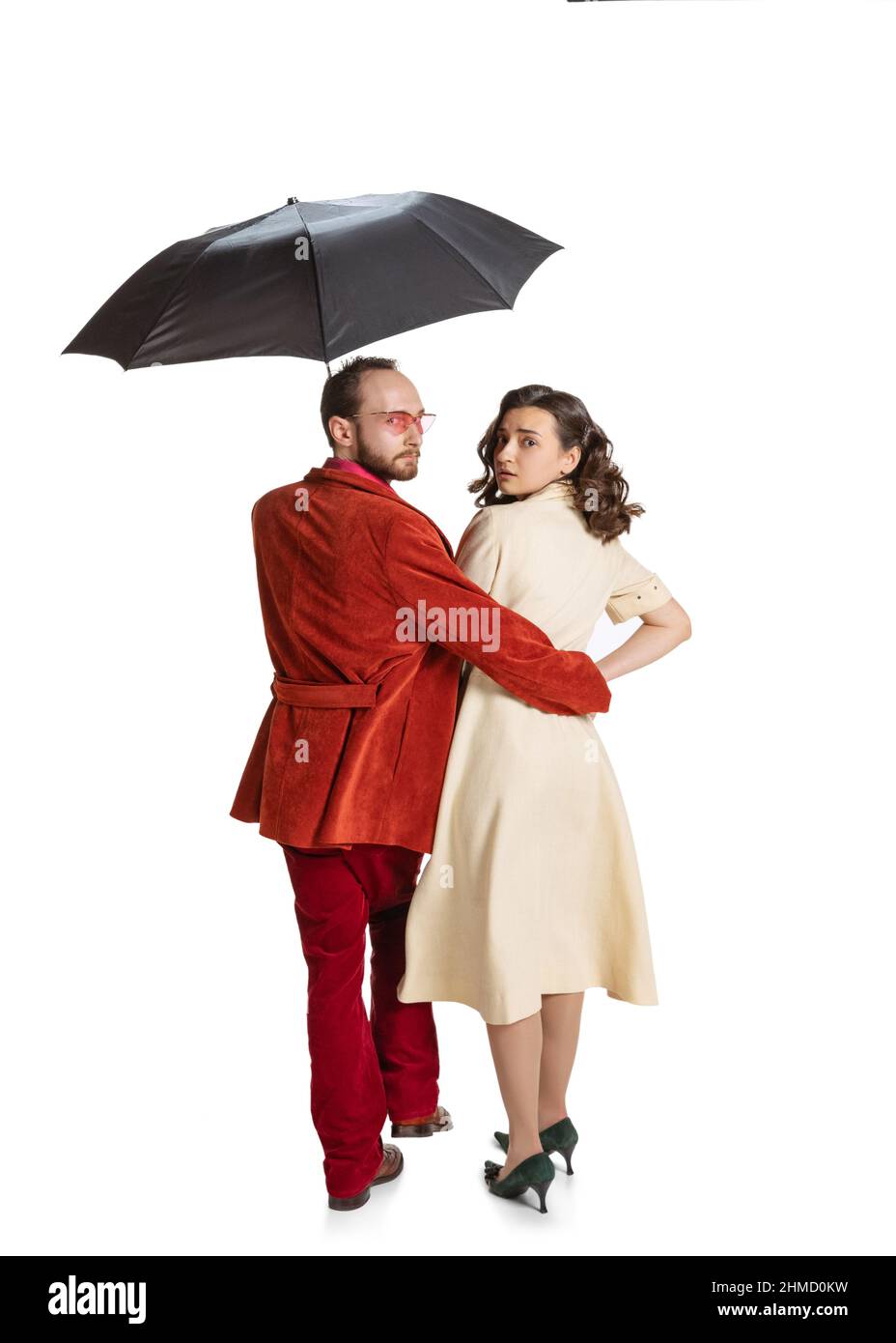 Giovane coppia familiare, uomo e donna in stile retrò abiti luminosi, moda di 70s, 60s anni a piedi con ombrello isolato su sfondo bianco studio Foto Stock