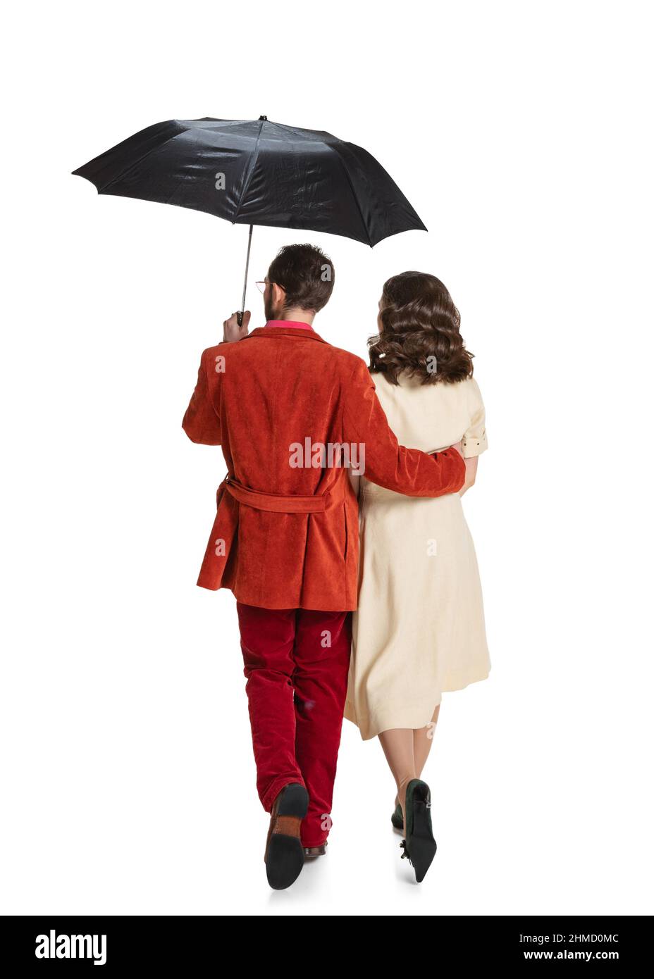 Vista posteriore di giovane coppia familiare, uomo e donna in stile retrò abiti luminosi, moda di 70s, 60s anni a piedi con ombrello isolato su bianco Foto Stock