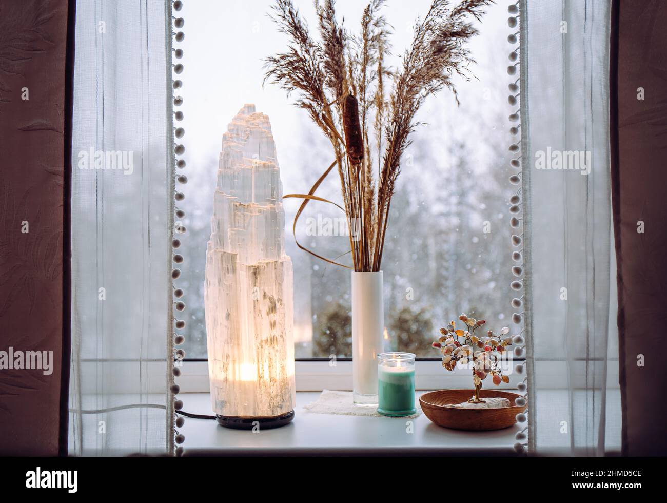 Ruvida grande selenite torre palo lampada illuminata sulla soglia della finestra di casa, spirituale decorazione accento casa. Inverno foresta sullo sfondo. Foto Stock