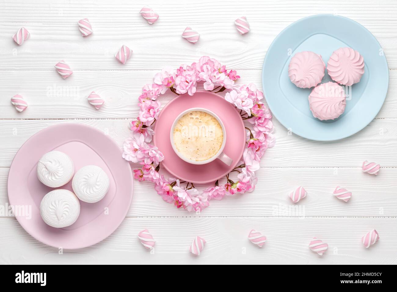 Tazza di caffè e fiori primaverili. Dessert al mattino per colazione, vista dall'alto. Fiore di ciliegio su un tavolo di legno bianco. Design piatto. Colore pastello Foto Stock