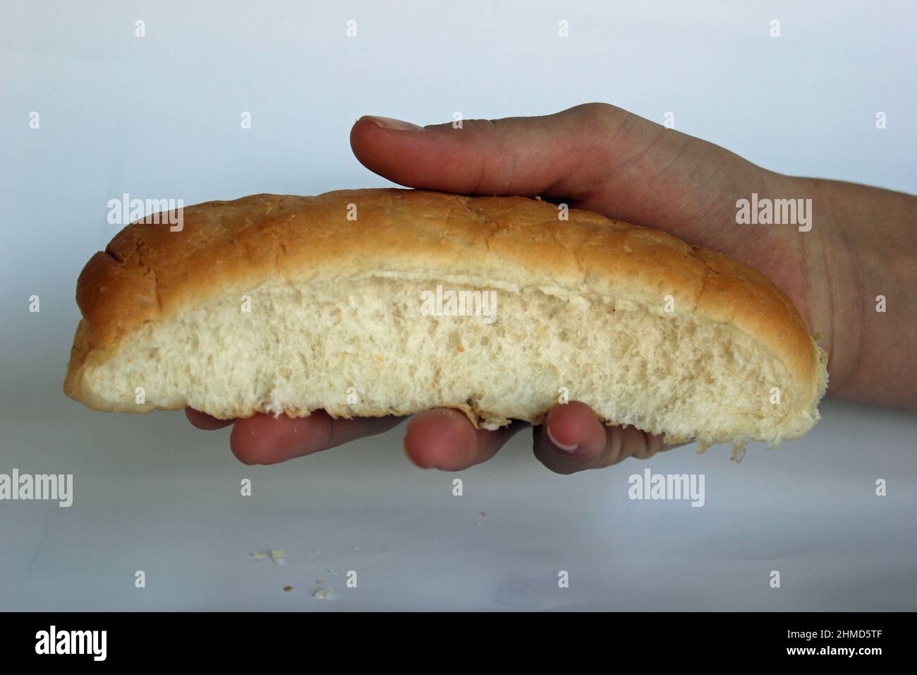 Solo mano azienda hotdog bun o un pezzo di pane come offerta per i bisognosi o affamato, con le briciole che giace nella parte anteriore, Foto Stock