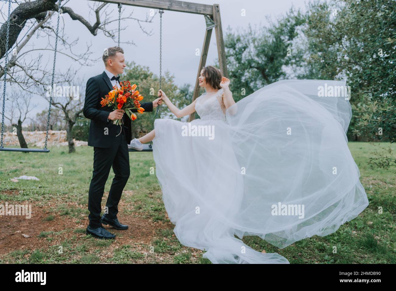 Felice coppia sorridente di stile che cammina in Toscana, Italia il giorno del matrimonio. SPOSI NOVELLI CON L'ALTALENA NEL PARCO. La sposa e lo sposo camminano giù il Foto Stock