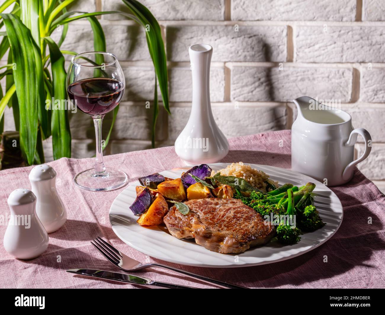 Bistecca di manzo con un bicchiere di vino rosso servito con broccolini, riso e patate arcobaleno al forno, primo piano Foto Stock