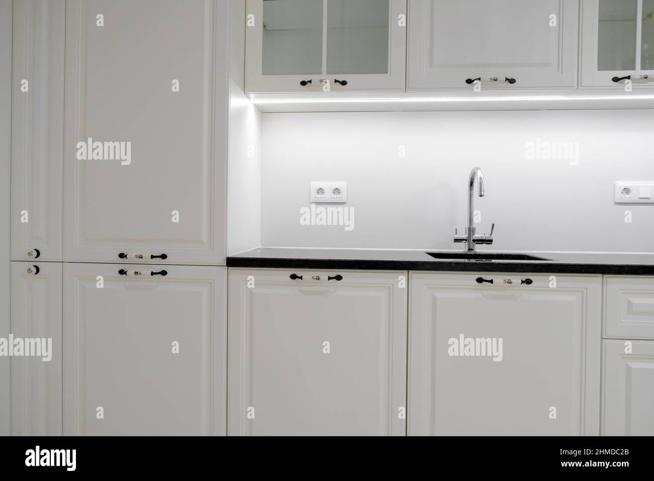 Cucina moderna ed elegante con cassetti e armadi bianchi, piano di lavoro in marmo nero e lavabo incassato con rubinetto d'argento Foto Stock