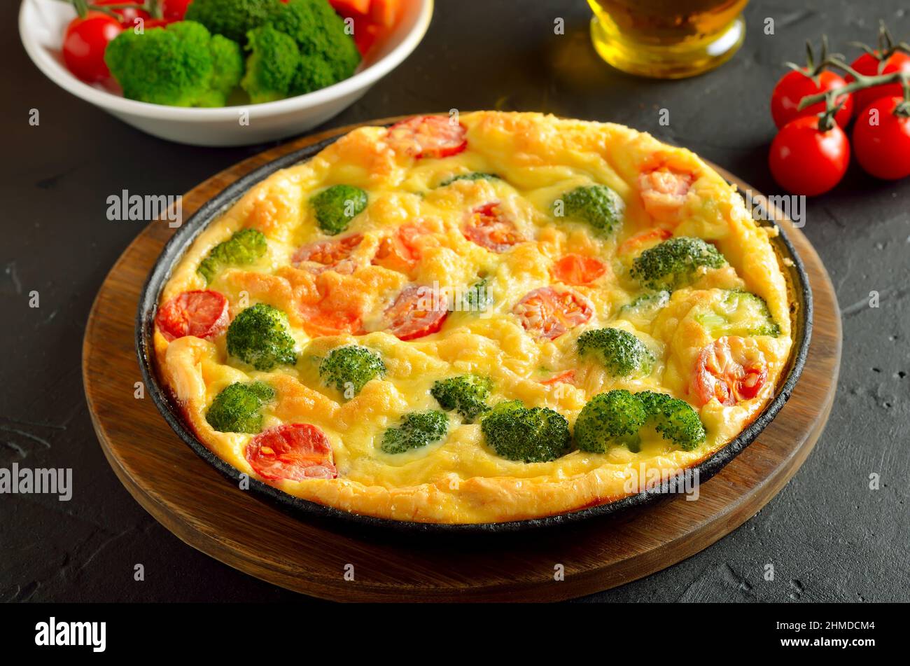 Frittata con broccoli e pomodori su sfondo di pietra scura Foto Stock