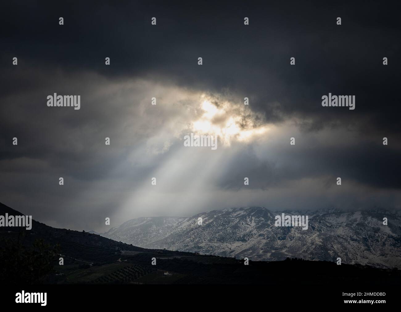 Vista maestosa della luce del sole che si infrangono attraverso la nuvola nuvolosa sulle montagne innevate Foto Stock