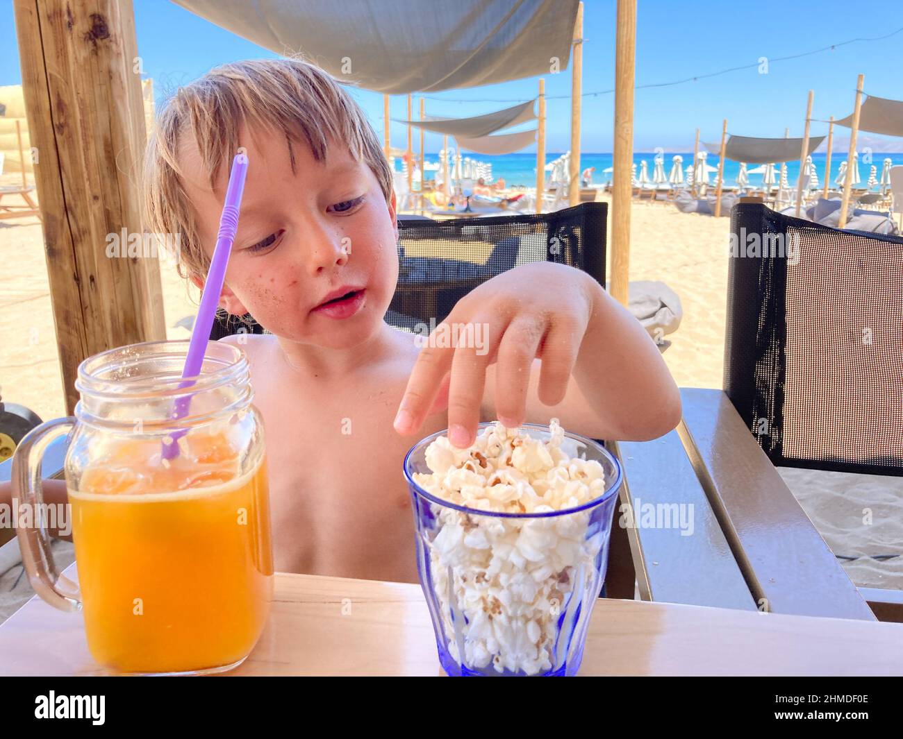 Ragazzo bevendo succo e mangiando popcorn mentre si rilassa in spiaggia Foto Stock