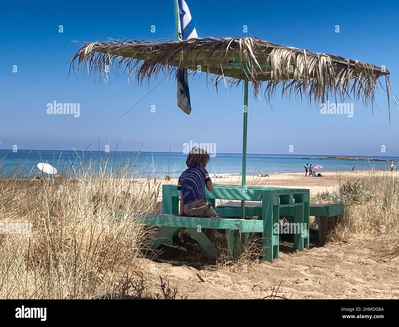 Vista posteriore del ragazzo seduto sul panca del caffè all'aperto contro il mare Foto Stock