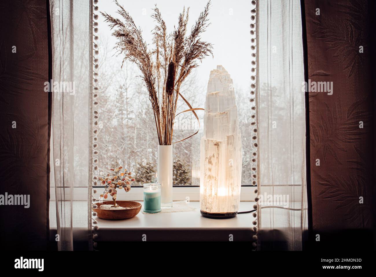 Ruvida grande selenite torre palo lampada illuminata sulla soglia della finestra di casa, spirituale decorazione accento casa. Inverno foresta sullo sfondo. Foto Stock
