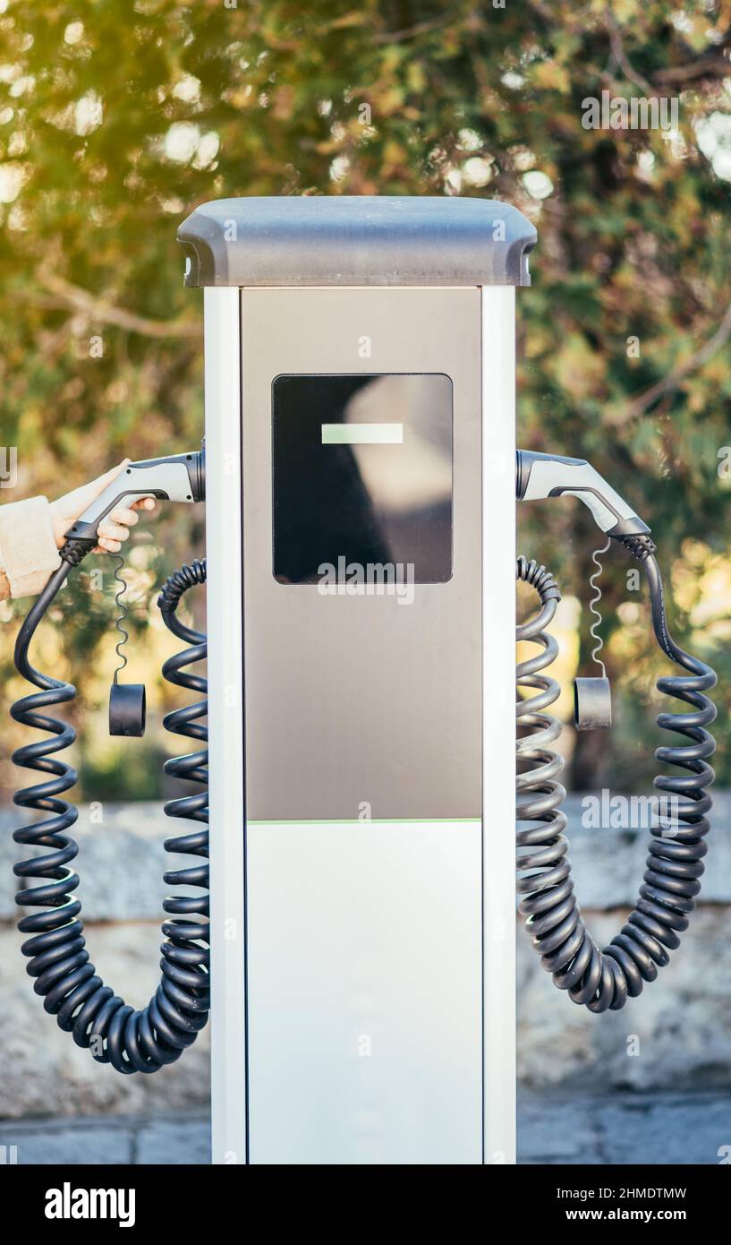 Donna irriconoscibile che tiene in mano una presa del caricabatteria per auto elettrica. Immagine verticale con profondità di campo poco profonda Foto Stock