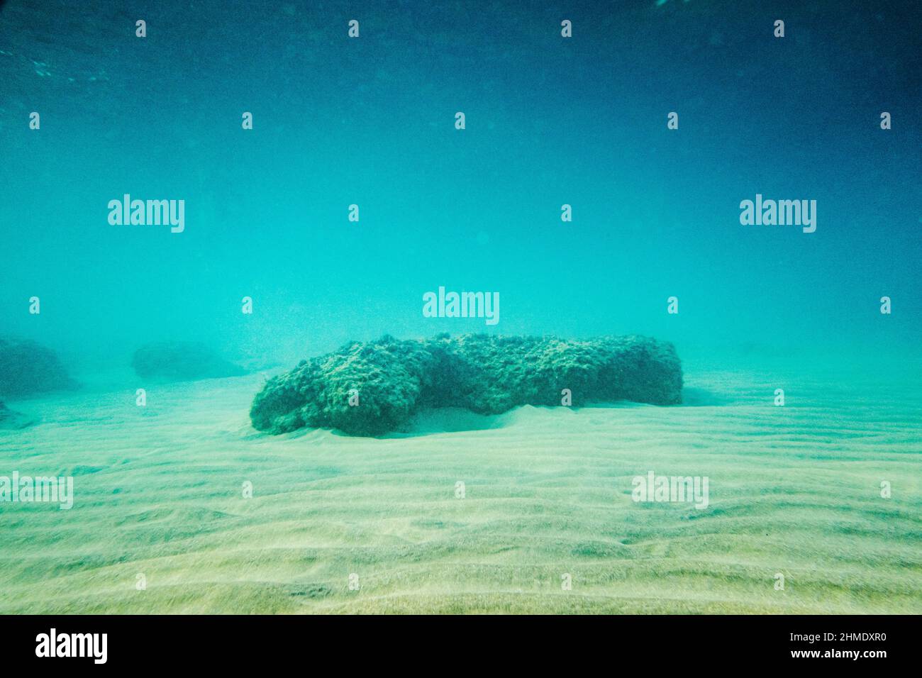 Rocce su sabbia increspata in acqua limpida blu Foto Stock