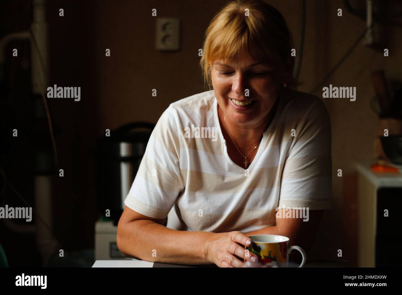 Defocus felice giovane donna caucasica sorridente mentre si siede a casa con caffè o tè tazza. Mattina di routine in cucina. Stile di vita domestico. Felice 40 anni w Foto Stock