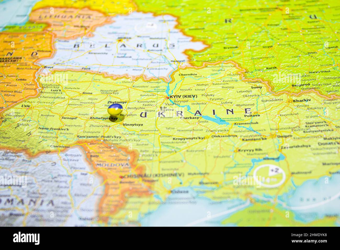 Bandiera nazionale ucraina fissata sulla mappa dell'Europa. Macro primo piano immagine del paese Ucraina su una mappa del mondo colorata e sfocata con attenzione al capitale Foto Stock