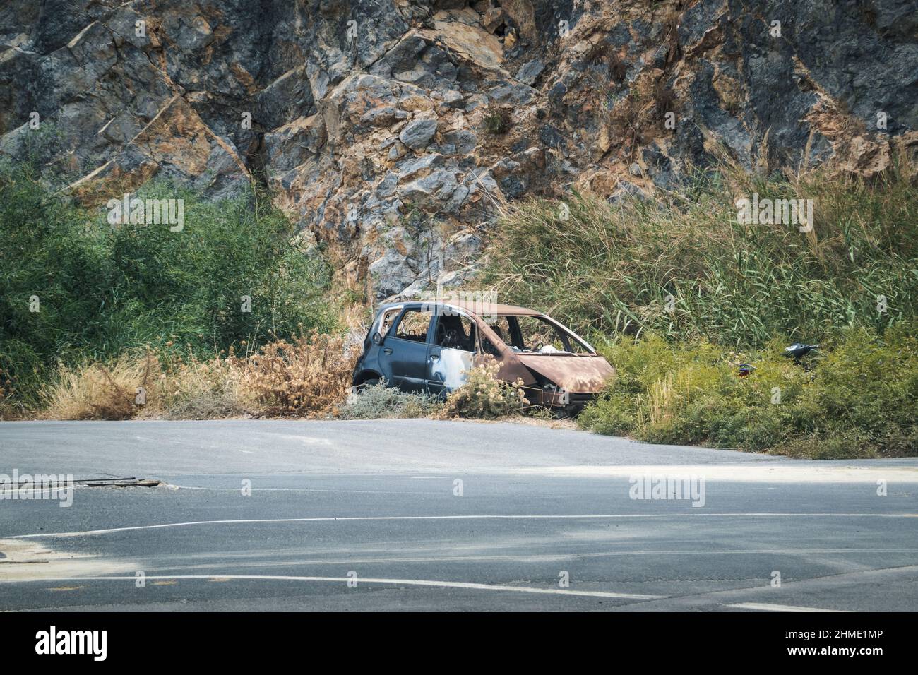 Vecchia macchina rotta accanto alla strada contro formazioni rocciose Foto Stock