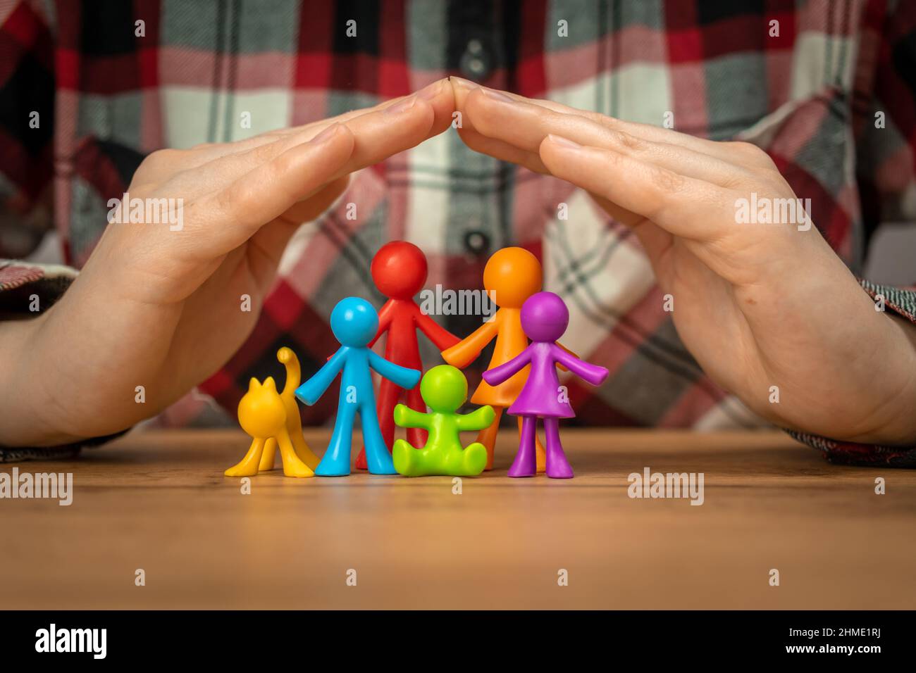 Concetto di assicurazione di famiglia con figurine di famiglia colorate coperte da mani su un tavolo di legno. Sicurezza e supporto Foto Stock