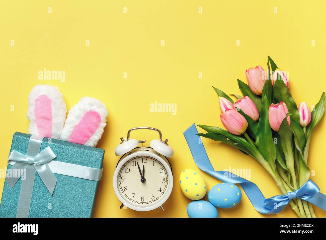 Uova di Pasqua sveglia bouquet di tulipani regalo rosa con orecchie di coniglio su sfondo giallo. Vista dall'alto dello spazio di copia a disposizione piatta. Foto Stock