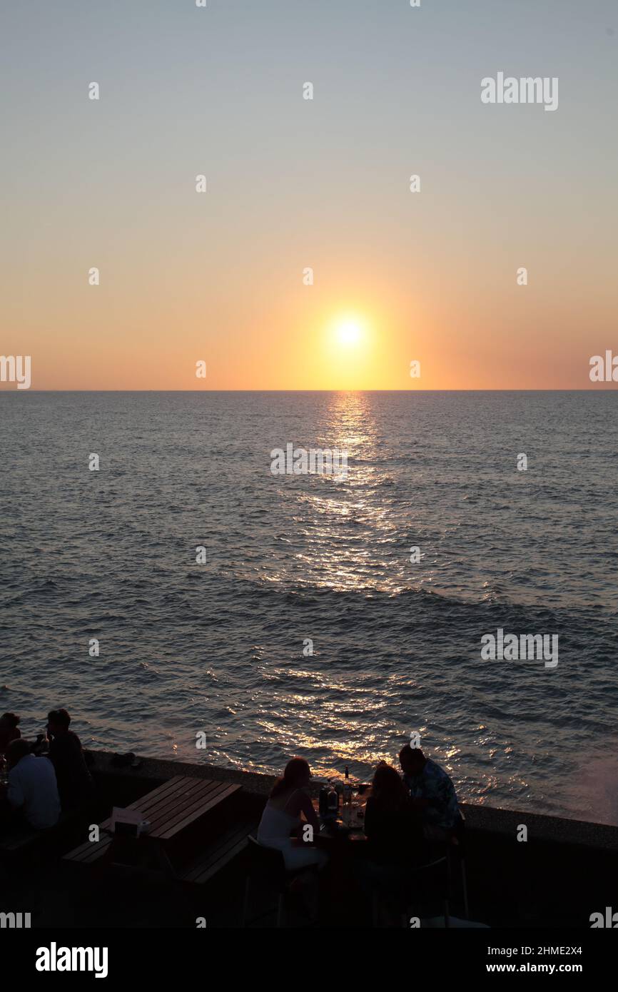 Le persone si godono un drink / mangiare all'aperto mentre si guarda il sole tramontare sull'oceano Atlantico a Bidart, Pays Basque, Francia Foto Stock