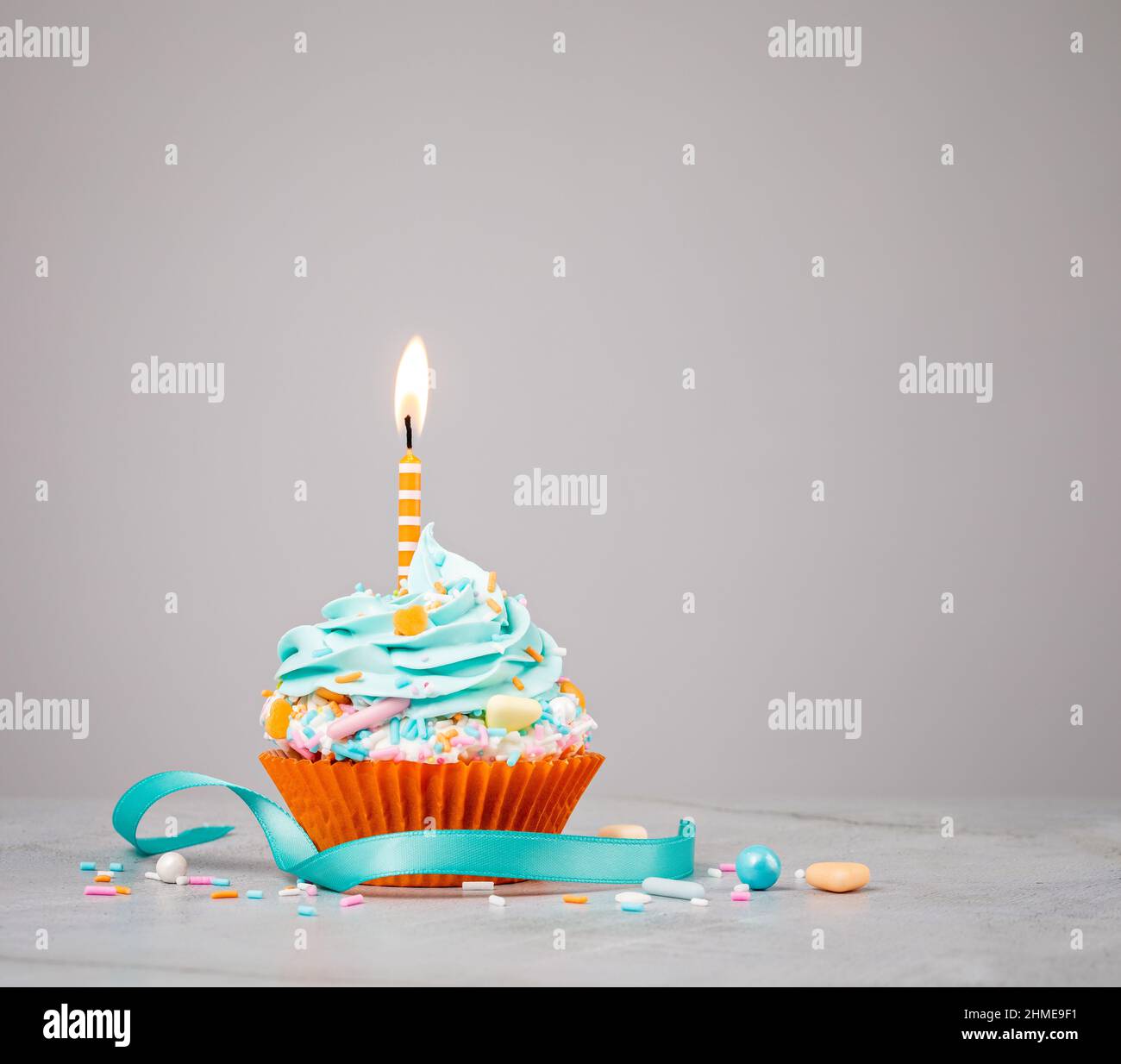Cupcake Blue Birthday con una candela arancione, spolverare e nastro su sfondo grigio chiaro. Foto Stock