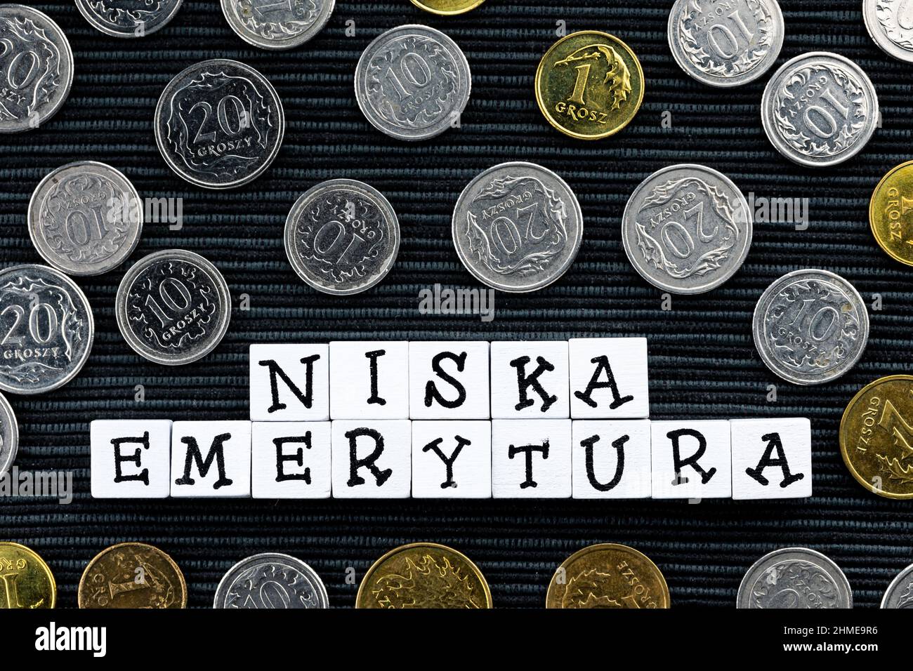 La dicitura 'niska emerytura' tradotta come 'low Pension' e molte monete polacche su sfondo nero. Nuove norme fiscali in Polonia. Foto scattata und Foto Stock
