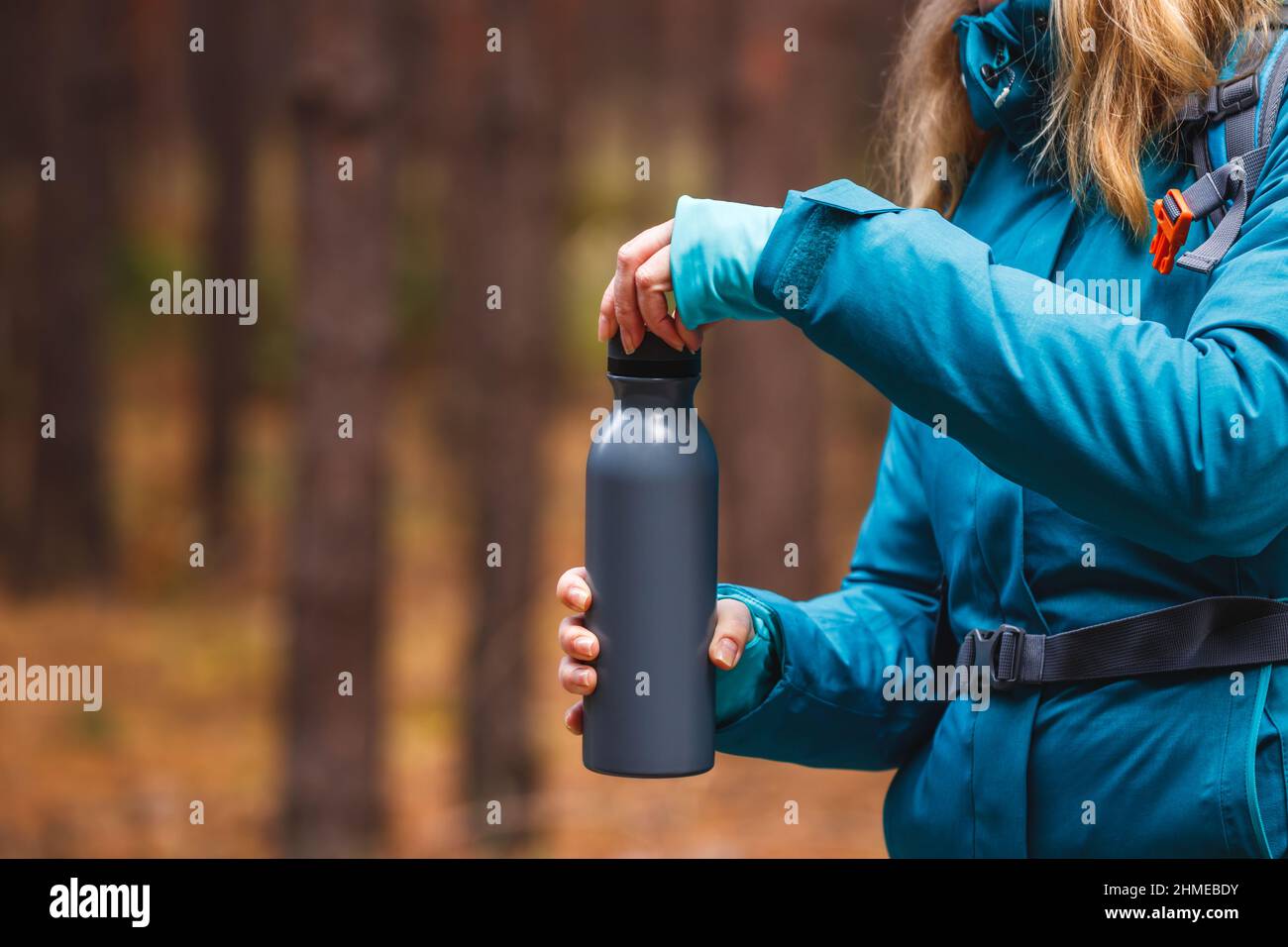 Bottiglia di thermos di apertura dell'escursionista con bevanda calda durante il trekking nella foresta. Campeggio e rinfresco durante l'escursione in bosco Foto Stock