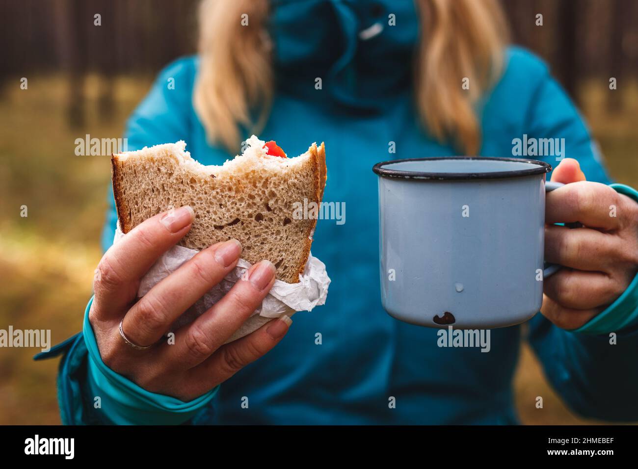 Rinfresco durante l'escursione nella natura. Donna che mangia sandwich e beve una bevanda calda. Escursionista che pranza all'aperto Foto Stock