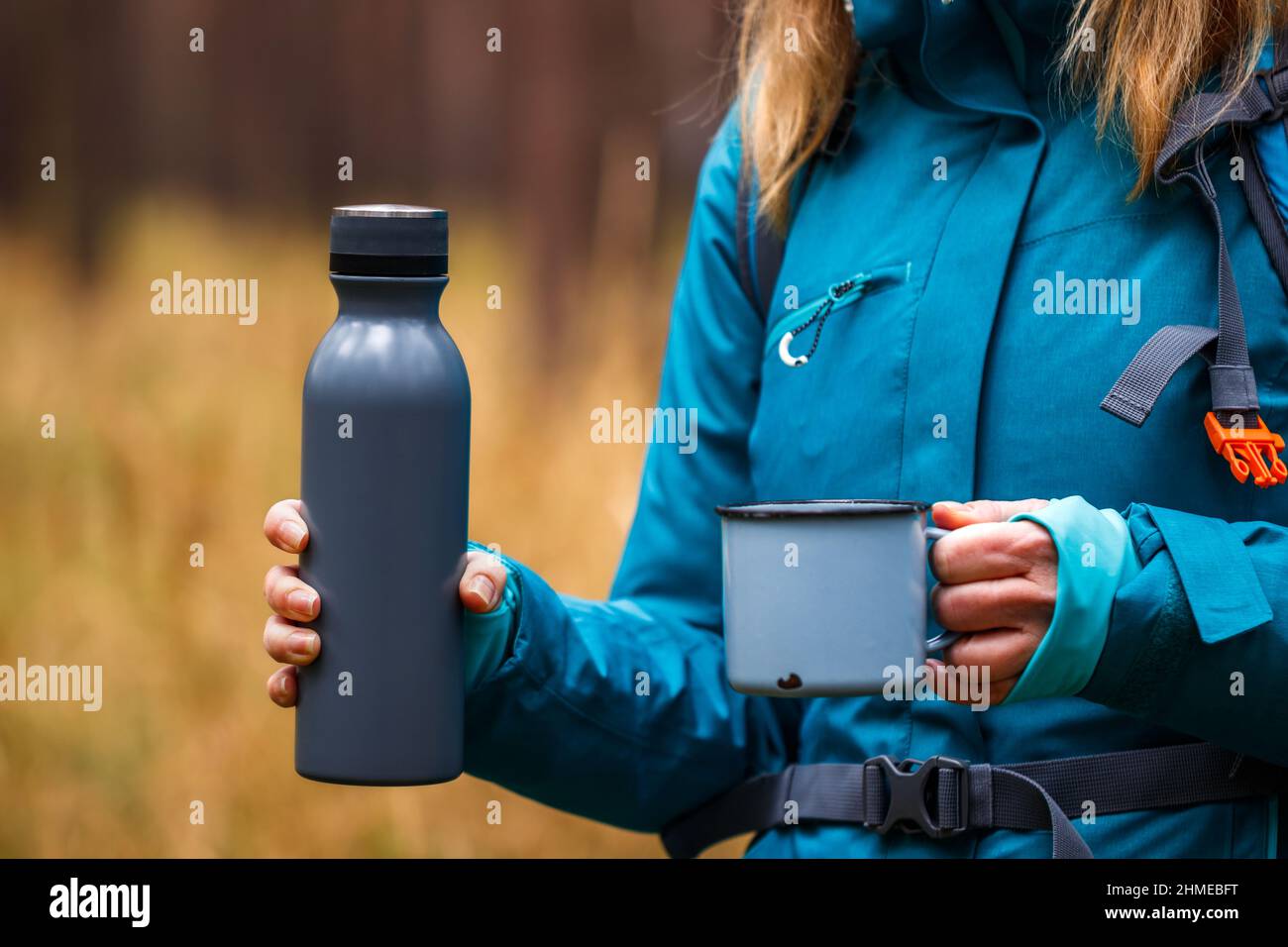 Donna escursionista che tiene thermos con bevanda calda e tazza di viaggio nella foresta. Donna escursioni e campeggio all'aperto Foto Stock