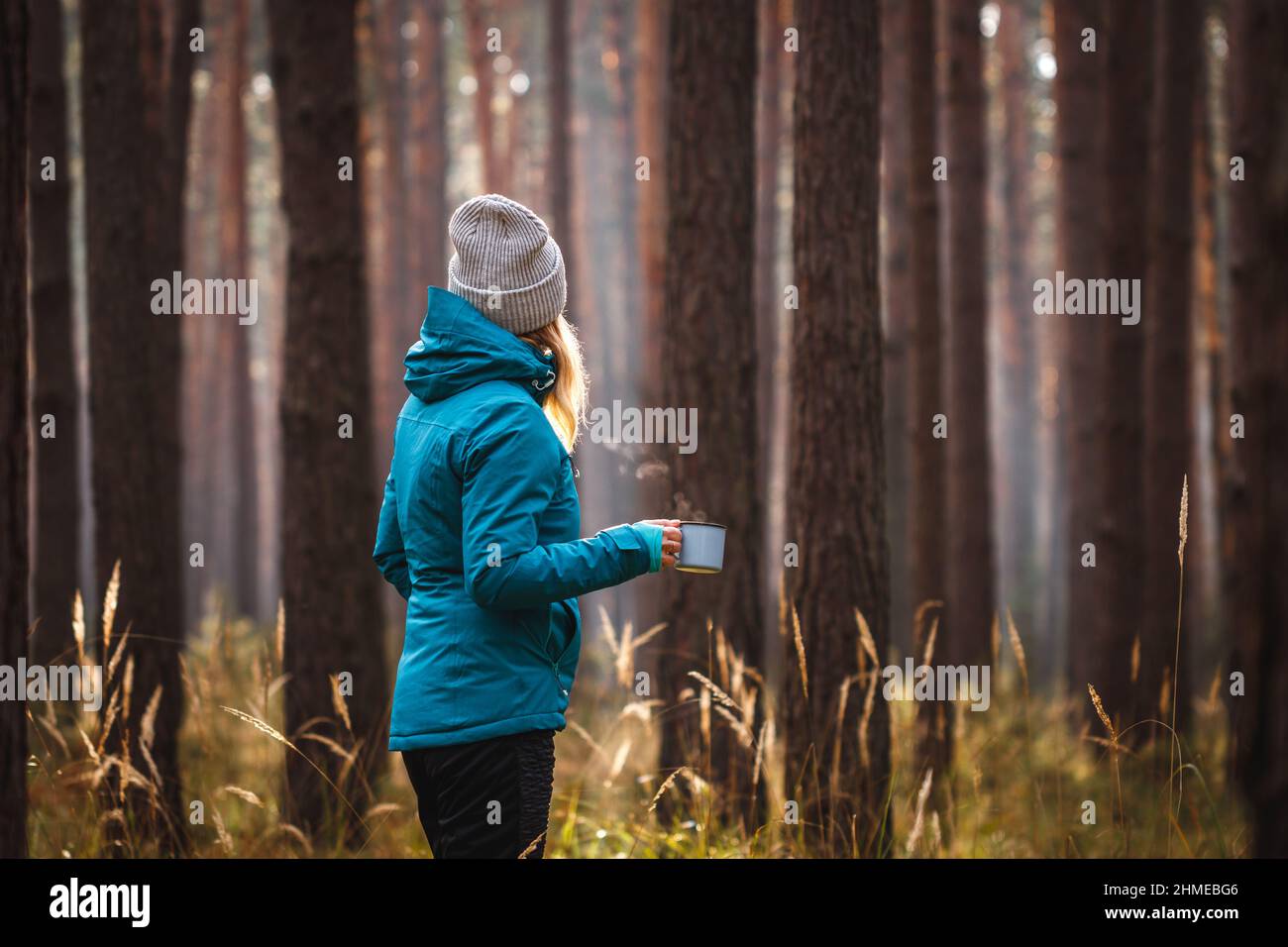 Donna che gode di bevanda calda durante le escursioni nella foresta al mattino freddo. Riposarsi e rilassarsi con un caffè all'aperto Foto Stock