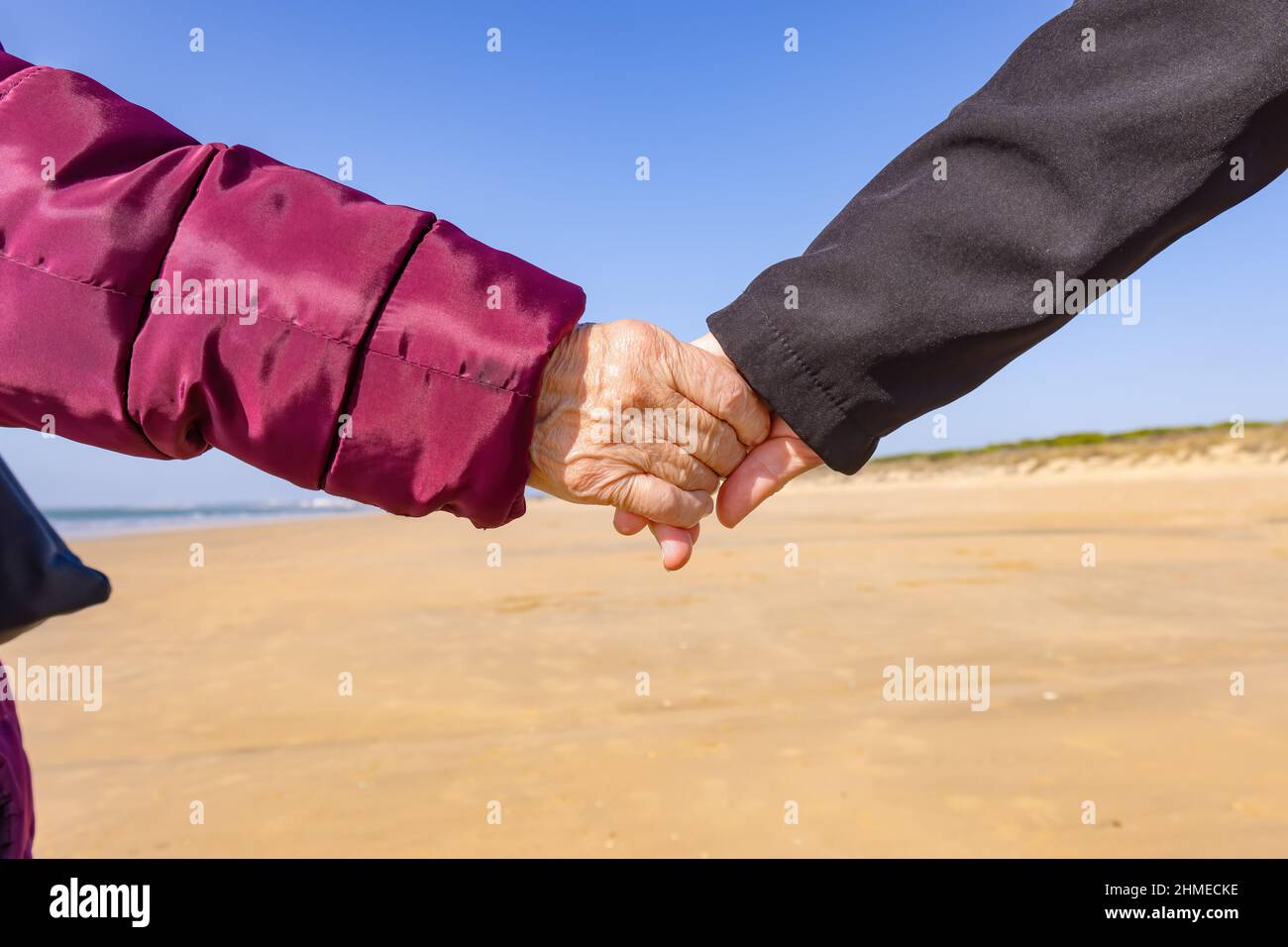 Una donna matura tiene la mano della madre anziana mentre cammina vicino alla spiaggia Foto Stock