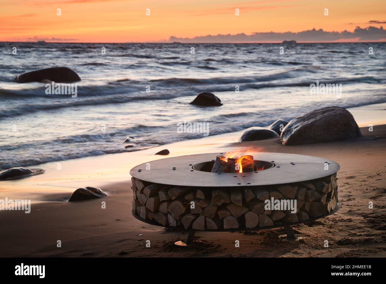Il bel metallo attorno a un camino sorge sulla costa sabbiosa con un'onda marea al tramonto, pietre, sabbia, onde, il paesaggio, tranquillità, sole Foto Stock