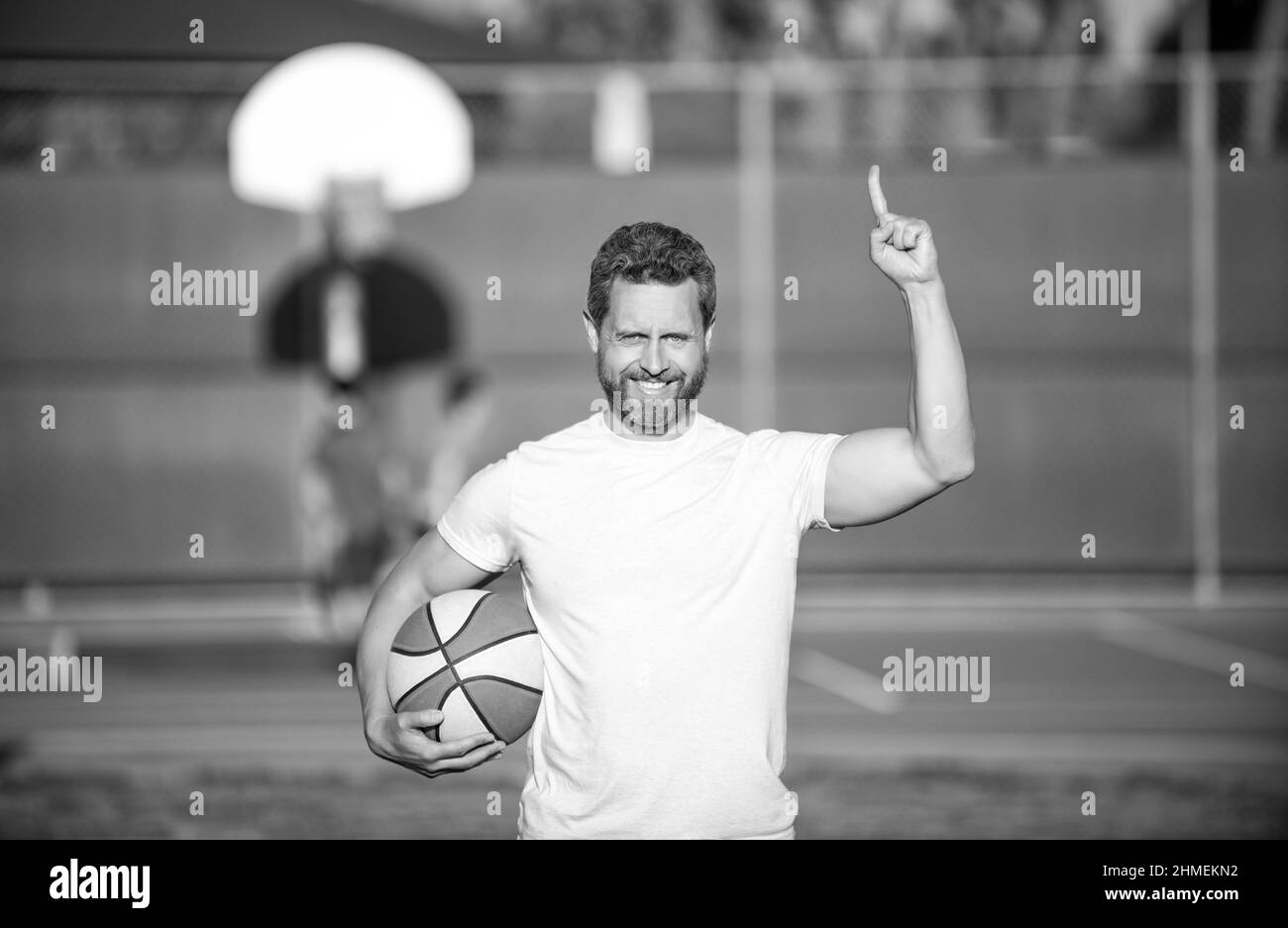 felice uomo muscoloso sportivo basket giocatore sollevato dito tenere palla all'aperto, sport Foto Stock